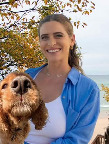 Female trainer from Beachside Dog Training holding a brown dog near the beach with autumn-colored trees in Huntington Beach, Orange County.